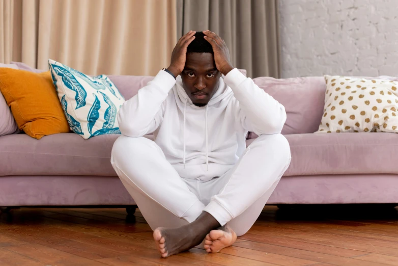 a man sitting on the floor in front of a couch, trending on pexels, renaissance, smooth white tight clothes suit, stressed out, african man, wearing a hoodie