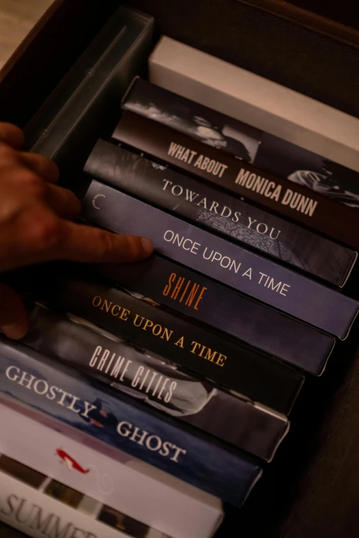 a person reaching for a stack of books, an album cover, by Dan Content, pexels contest winner, serial art, 1 3 ghosts movie artwork, high angle close up shot, dvd package, once upon a time