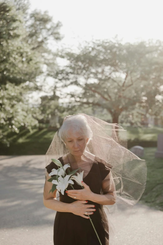 a woman in a black dress holding a bouquet of flowers, cementary, ray of light through white hair, funeral veil, 2019 trending photo