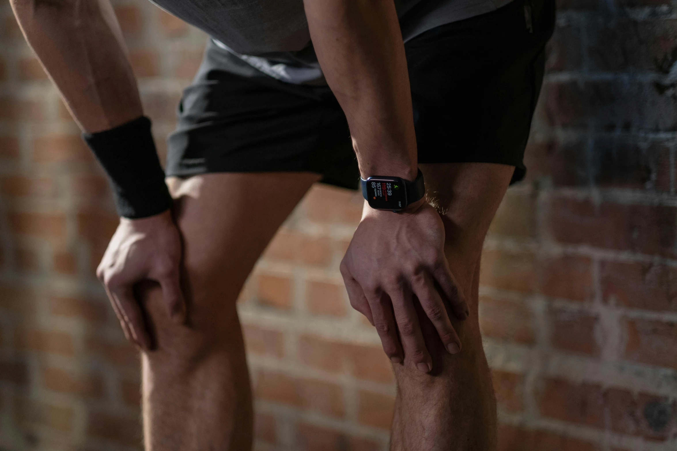 a man standing on a skateboard in front of a brick wall, by Adam Marczyński, trending on pexels, renaissance, hugging his knees, in a gym, swollen veins, black bandage on arms