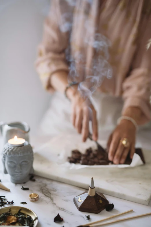 a close up of a person preparing food on a table, incense, chocolate, profile image, grey