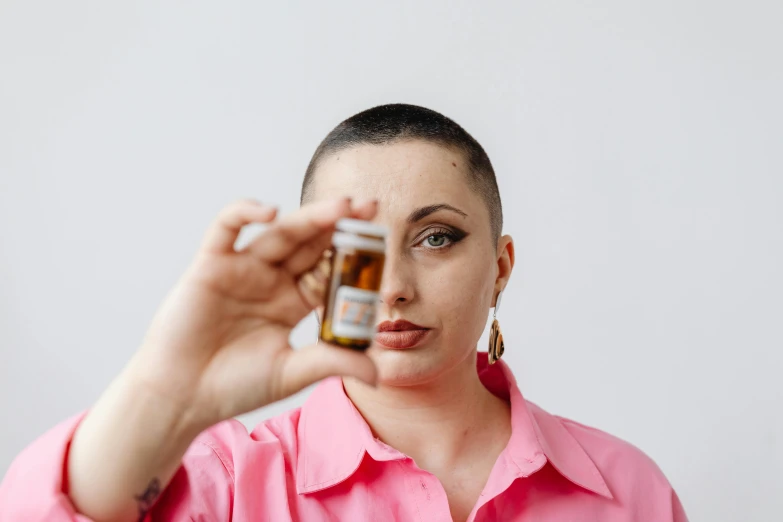 a woman taking a picture with her cell phone, an album cover, by Winona Nelson, antipodeans, shaved head, offering the viewer a pill, portrait featured on unsplash, holding a bottle