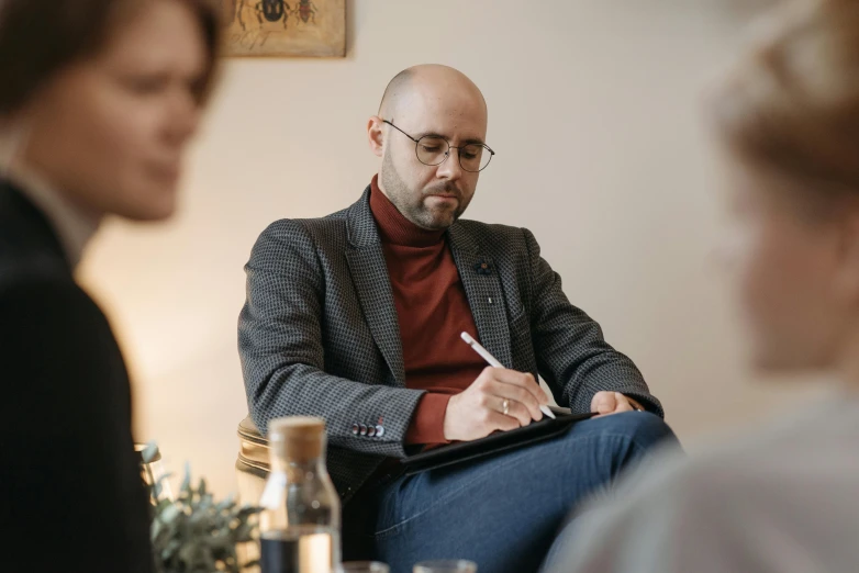 a man sitting in a chair with a pen in his hand, mental health, a group of people, profile image, brown