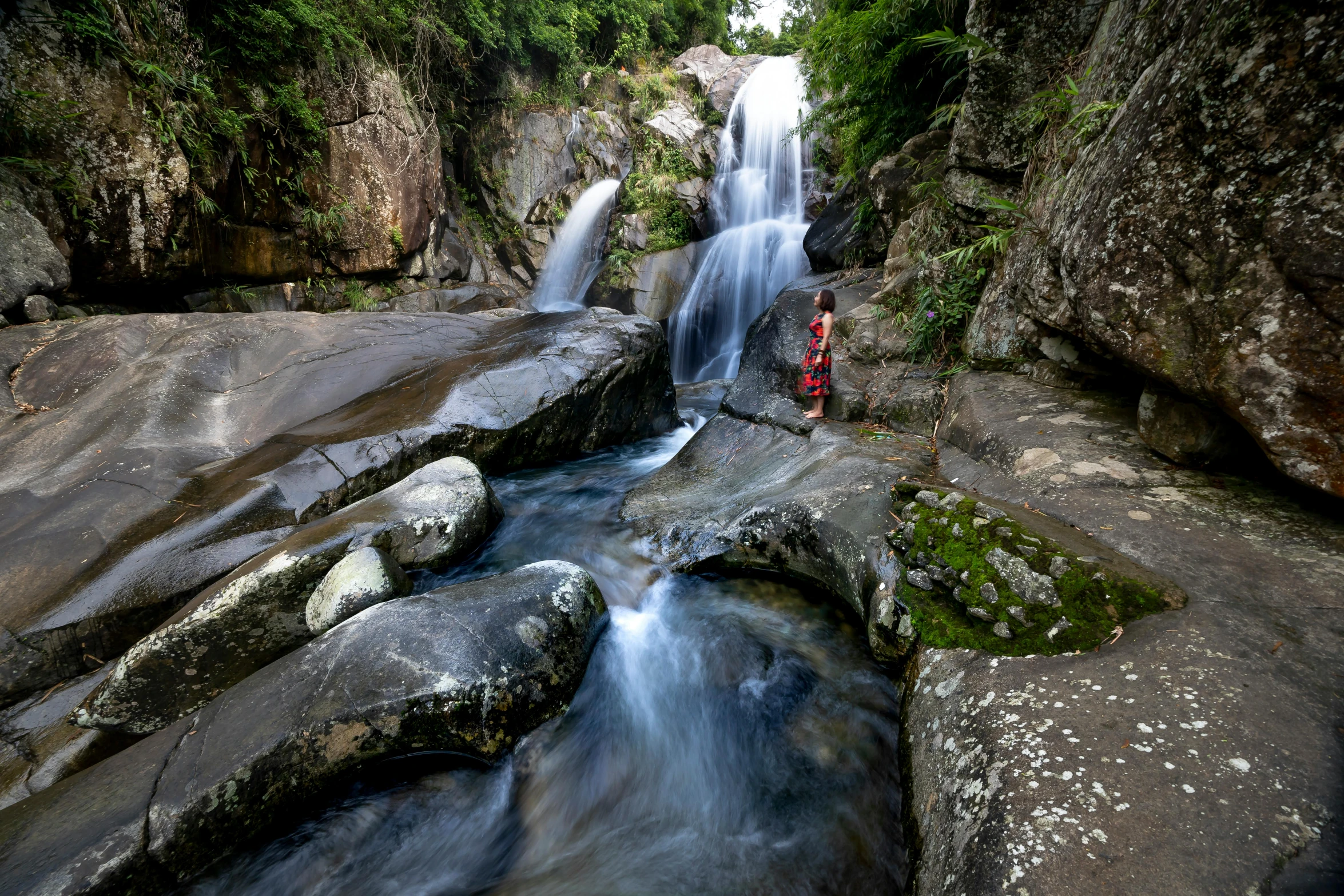 a man standing in front of a waterfall, by Peter Churcher, ultrawide image, boulders, shan shui, wide high angle view