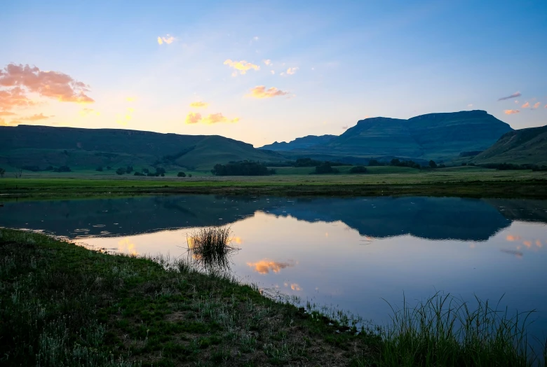 a body of water with a mountain in the background, by Arie Smit, pexels contest winner, standing in the grass at sunset, farms, small pond, at gentle dawn blue light