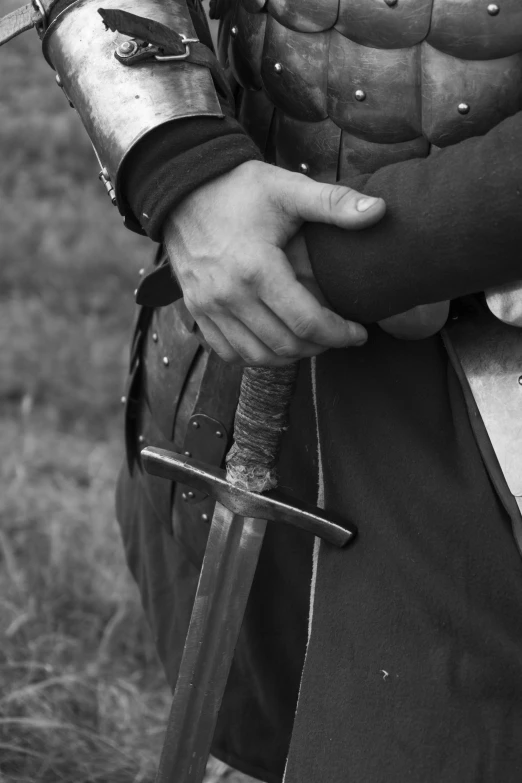 a man dressed in armor holding a sword, a black and white photo, inspired by Howard Pyle, unsplash, dressed in a [ [ 1 2 th century, low detail, hands of men, simple