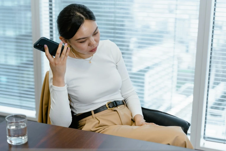 a woman sitting in a chair talking on a cell phone, inspired by Ruth Jên, trending on pexels, realism, office clothes, asian female, realistic »