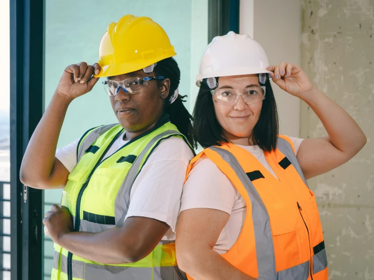 a couple of women standing next to each other, pexels contest winner, arbeitsrat für kunst, hard hat, diverse costumes, bright construction materials, wearing medium - sized glasses