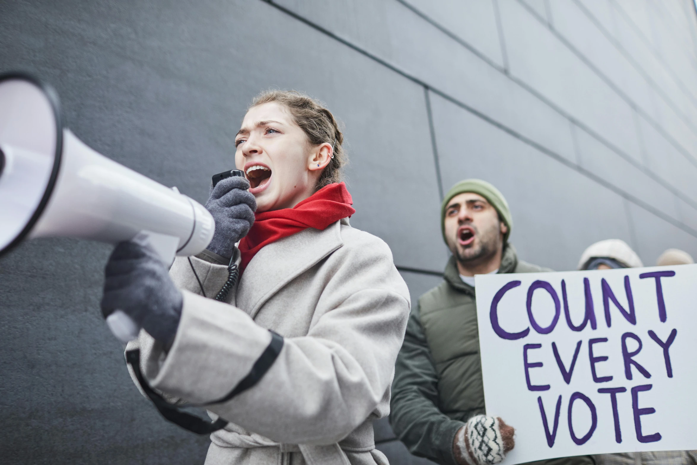 a woman holding a megaphone and a sign that says count every vote, by Itō Seiu, shutterstock, excessivism, model wears a puffer jacket, yelling, alessio albi, high quality photo