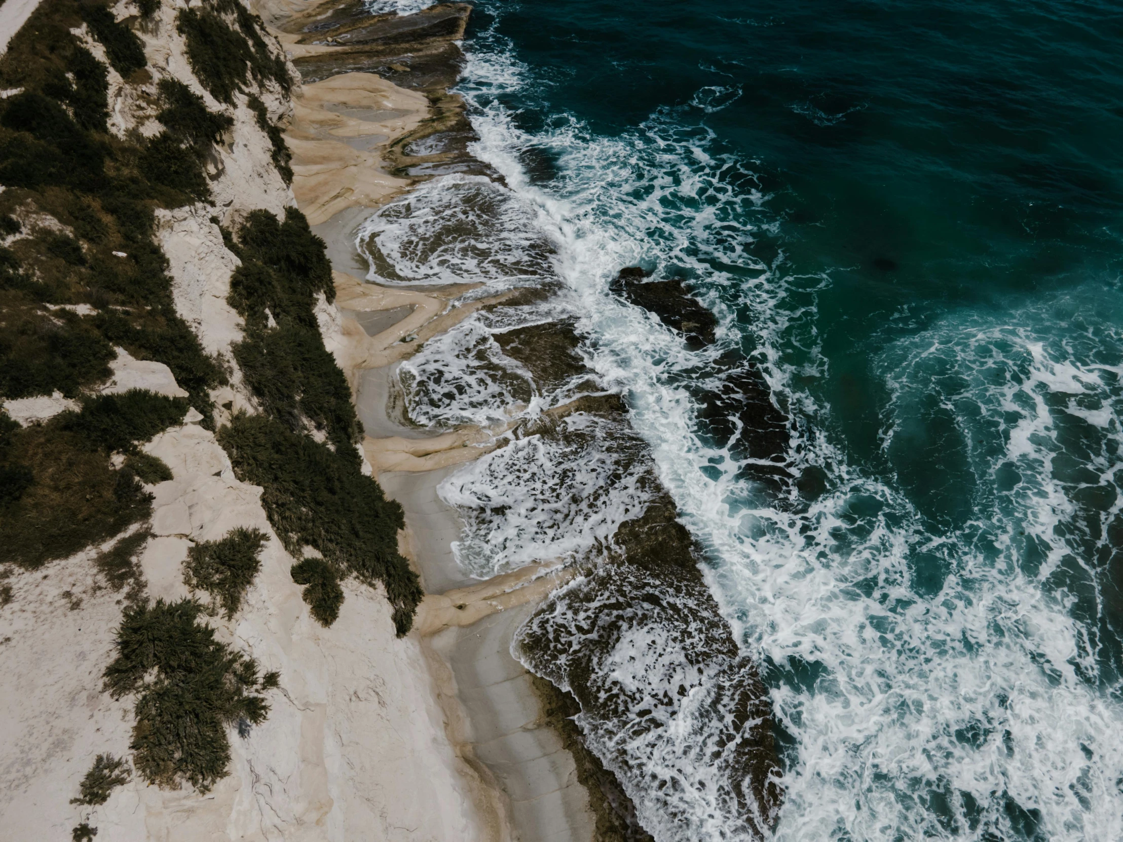 a large body of water next to a sandy beach, by Lee Loughridge, pexels contest winner, looking down a cliff, ocean spray, birdseye view, rippling muscles