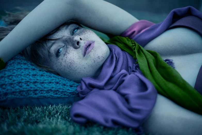 a woman laying on top of a lush green field, a colorized photo, inspired by Elsa Bleda, flickr, blue and purple, cold freezing nights, intense stare, freckle