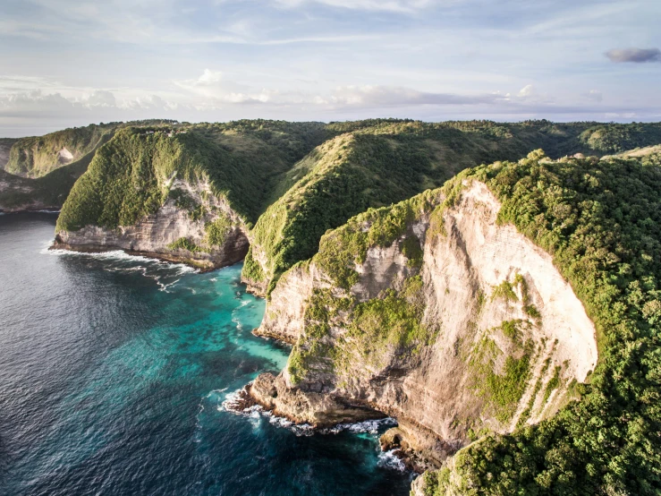 a large body of water next to a lush green hillside, by Jesper Knudsen, pexels contest winner, sumatraism, coastal cliffs, flying rocky island, conde nast traveler photo, over a chalk cliff