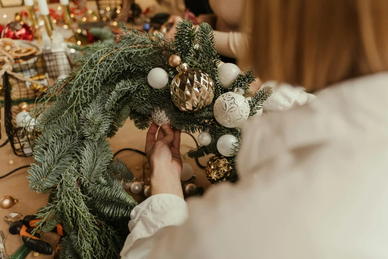 a close up of a person putting ornaments on a wreath, by Julia Pishtar, pexels contest winner, aleksandra waliszewska, tall, covered, how-to