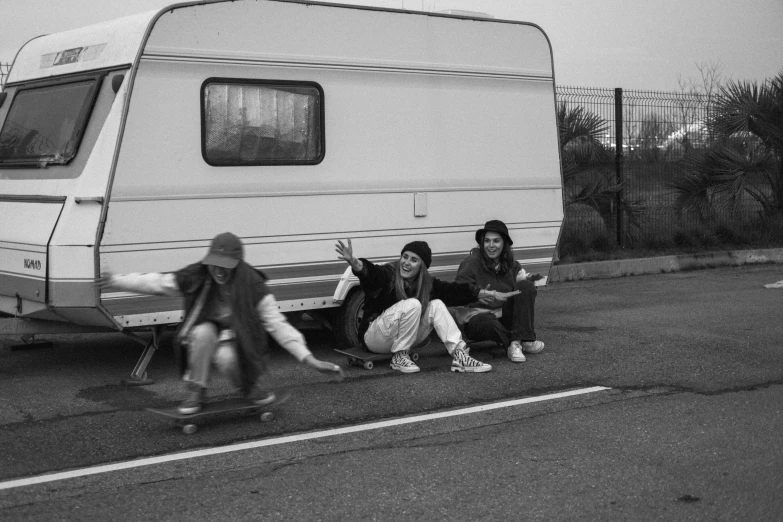 a group of people sitting on the side of a road, a black and white photo, by Nathalie Rattner, plays skateboards, caravan, dasha taran, carefree