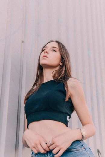 a woman standing in front of a metal wall, inspired by Elsa Bleda, unsplash contest winner, wearing a black cropped tank top, hailee steinfeld, sport bra and shirt, profile pic