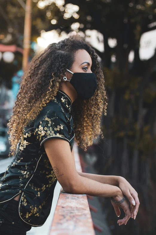 a woman with curly hair wearing a face mask, by Matt Cavotta, sitting, black and gold colors, chinese woman, in an urban setting