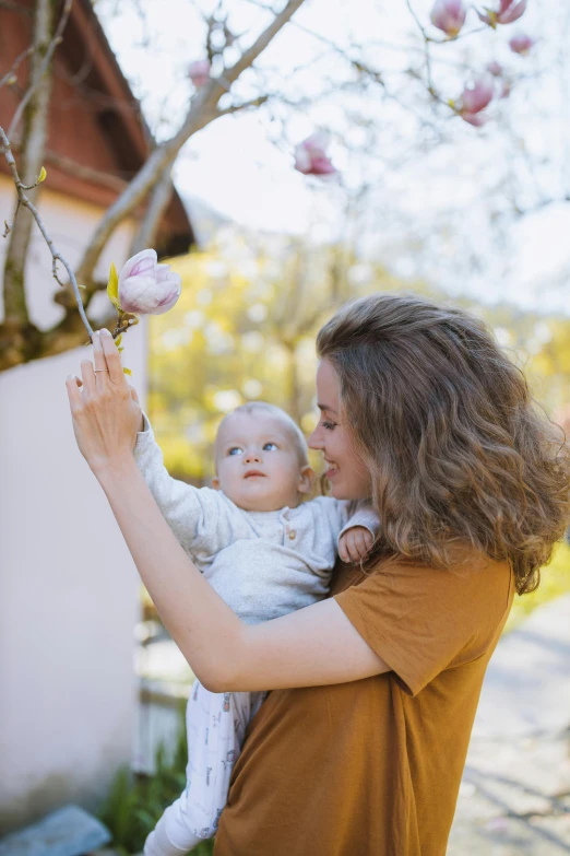 a woman holding a baby in her arms, pexels contest winner, happening, on a branch, holding a flower, square, high quality photo