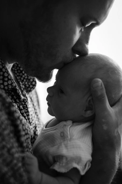 a man holding a baby in his arms, a black and white photo, by Matt Cavotta, kiss mouth to mouth, lachlan bailey, in 2 0 1 5, profile image