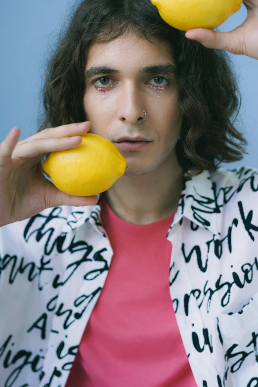 a man holding two lemons up to his face, an album cover, inspired by Davide Sasselli, looking away from camera, wearing a shirt, close - up photograph, close-up photograph