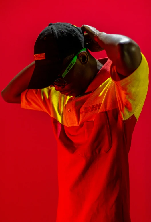 a man standing in front of a red wall, an album cover, inspired by Mike Winkelmann, pexels, neon visor, wearing polo shirt, ( ( dark skin ) ), gradient red to yellow