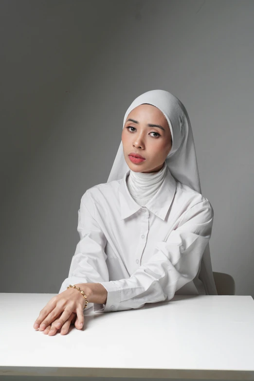 a woman in a white shirt sitting at a table, inspired by Nazmi Ziya Güran, hijab, xision wu, press shot, bella poarch