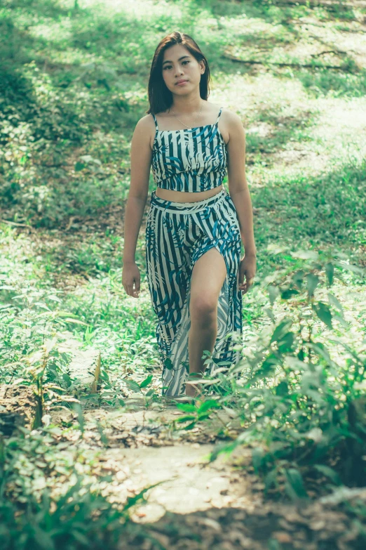 a woman walking down a path in the woods, an album cover, inspired by Samuel Silva, unsplash, renaissance, croptop, stripey pants, sukhothai costume, blues