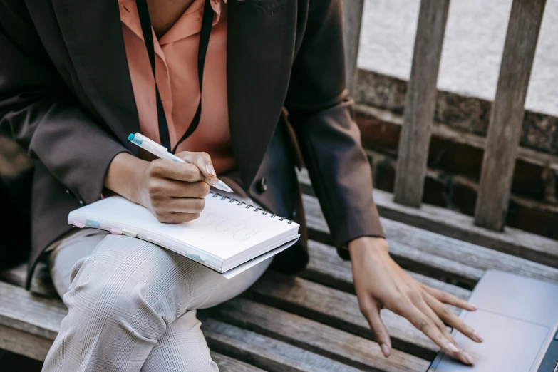 a woman sitting on a bench writing on a notebook, trending on pexels, business attire, thumbnail, a high angle shot, background image