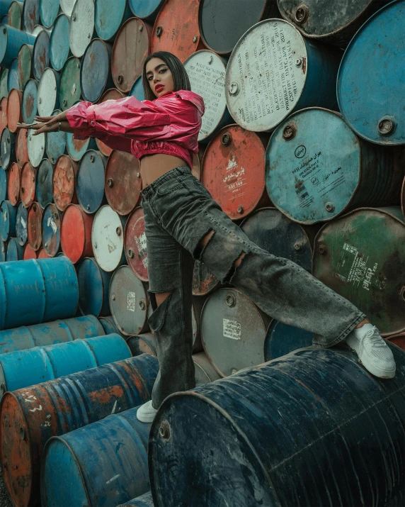 a man standing on top of a stack of barrels, an album cover, inspired by Elsa Bleda, trending on pexels, graffiti, female dancer, indonesia, non binary model, covered in oil