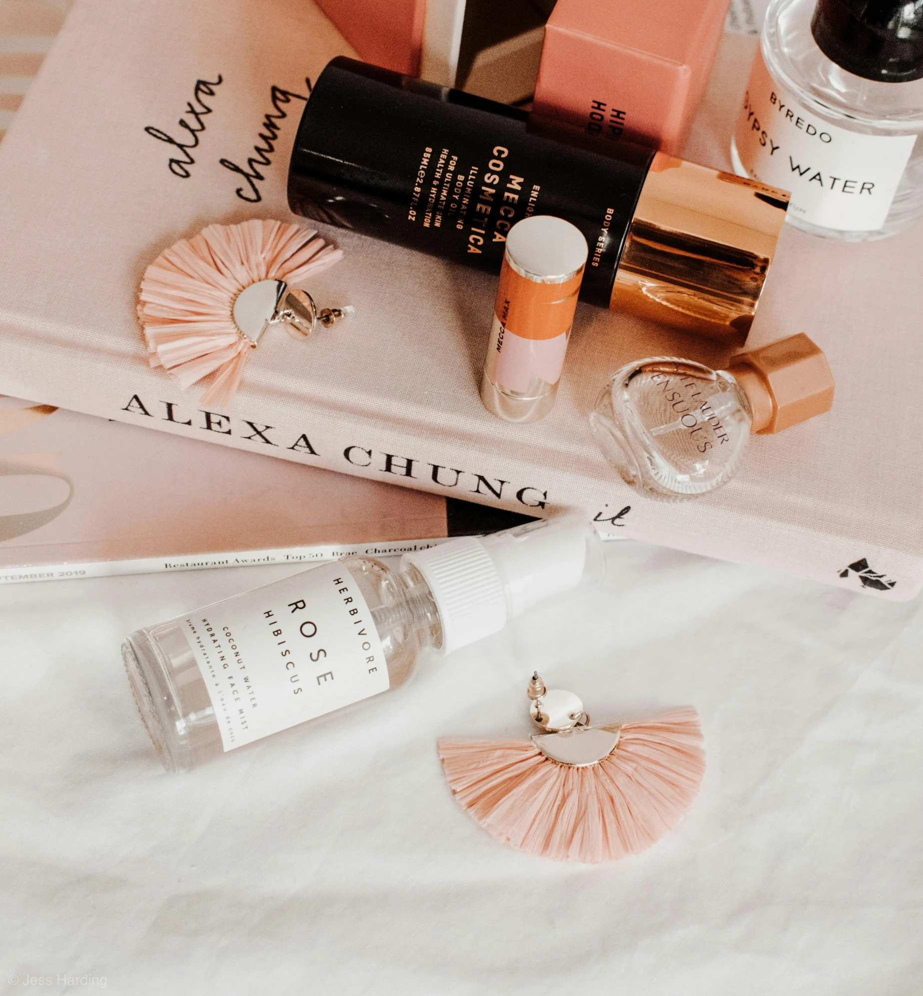 a stack of books sitting on top of a bed, by Olivia Peguero, pexels contest winner, aestheticism, perfume bottle, white and light-pink outfit, fan favorite, miniature product photo