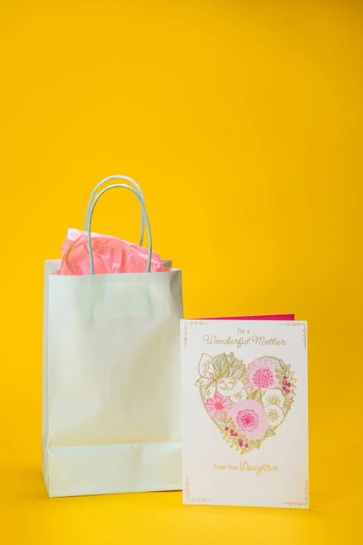 a bag and a card on a yellow background, by Julia Pishtar, greeting card, mother of pearl iridescent, f / 3, pink