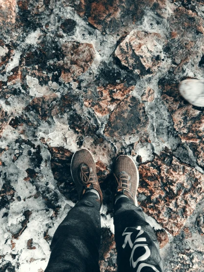 a person standing on top of a rock covered ground, cold as ice! 🧊, legs taking your pov, lots of embers, chocolate. rugged