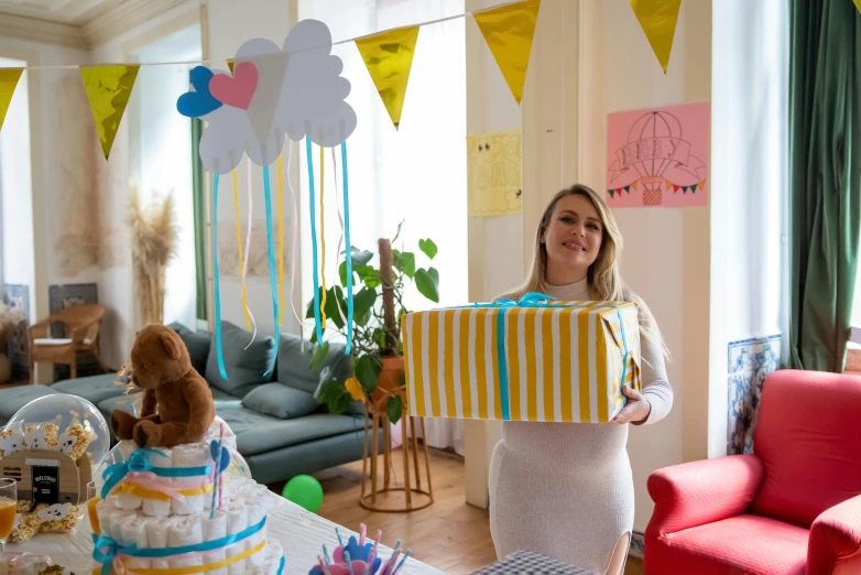 a woman standing in a living room holding a present, a cartoon, by Julia Pishtar, pexels contest winner, at a birthday party, maternity feeling, blue theme and yellow accents, romanian