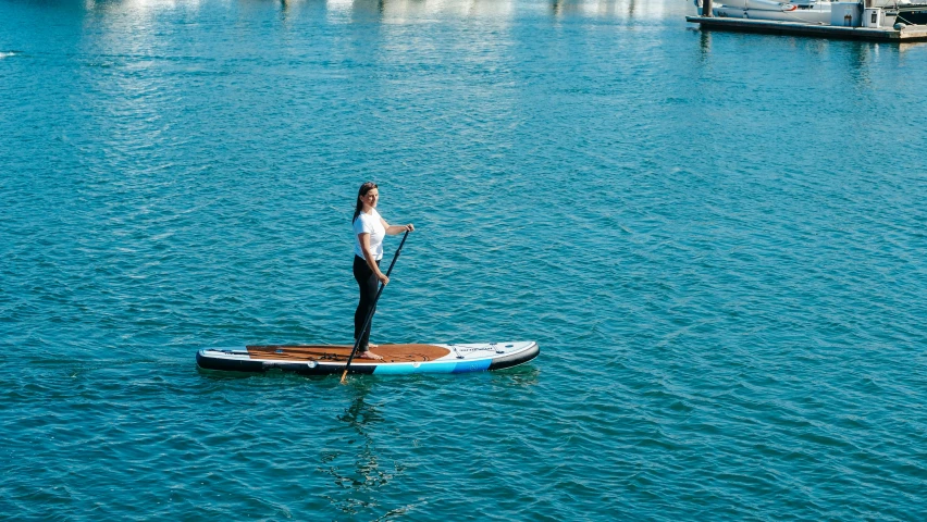 a man riding a paddle board on top of a body of water, blue water, boat, at the waterside, thumbnail