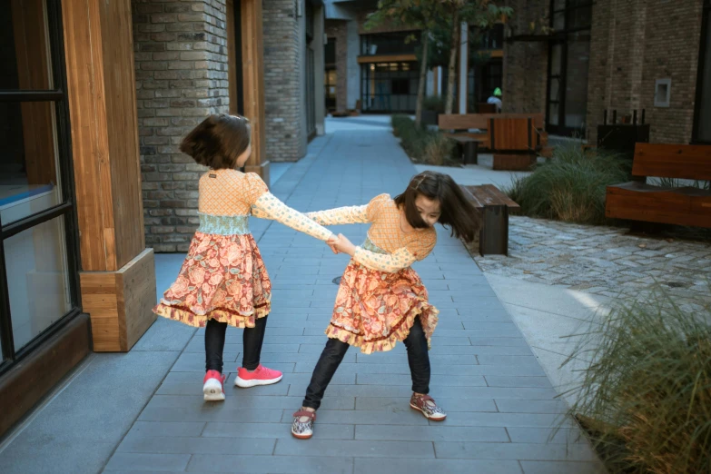 two little girls standing next to each other on a sidewalk, unsplash, interactive art, dancing a jig, patterned clothing, holding each other, programming