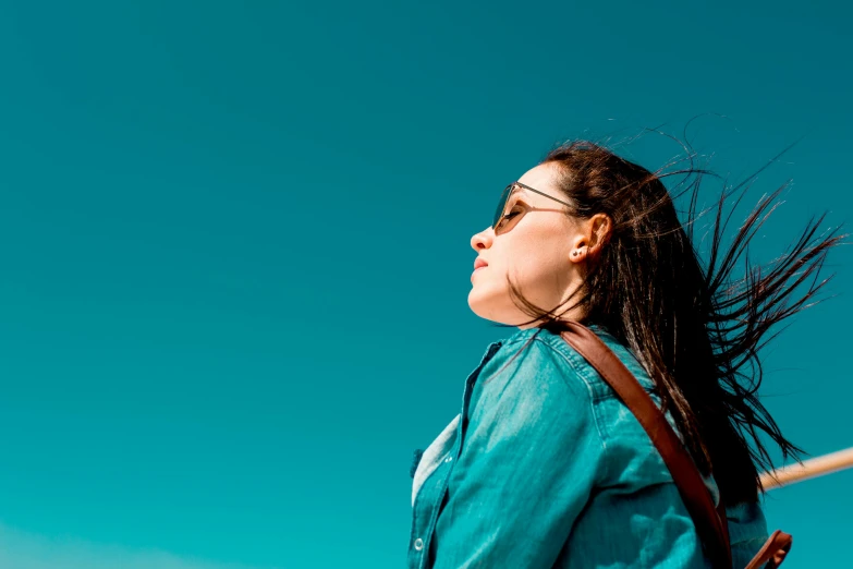 a woman in a blue shirt is flying a kite, pexels contest winner, gazing off into the horizon, avatar image, wearing blue sunglasses, profile view