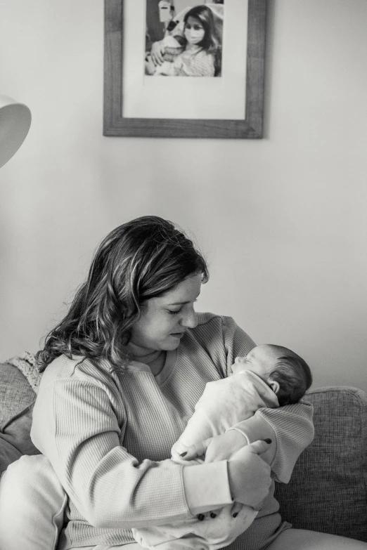 a woman sitting on a couch holding a baby, a black and white photo, by Ruth Simpson, pexels, profile picture, nursing, first light, indoor picture