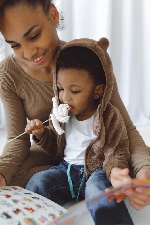 a woman and a child are sitting on the floor, an ewok eating a lollipop, marshmallows, stockphoto, african canadian