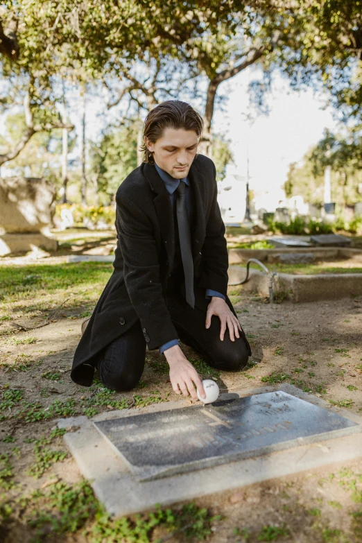 a man kneeling on the ground with a baseball in his hand, an album cover, by Winona Nelson, trending on reddit, auto-destructive art, standing over a tomb stone, a handsome, an elegant, julian ope