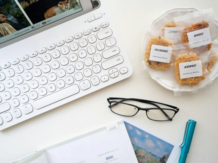 a laptop computer sitting on top of a white desk, a picture, by Jessie Algie, unsplash, snacks, wearing square glasses, ko-fi, white