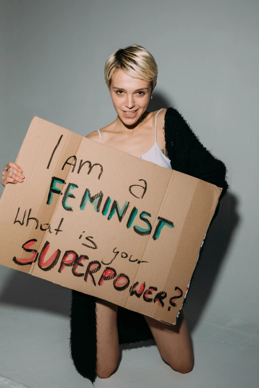 a woman holding a sign that says i am a feminist what is your superpower?, show, joel fletcher, lesbian, model posing