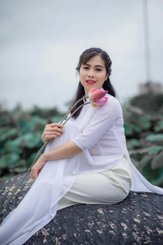 a woman sitting on a rock with a flower in her hand, inspired by Cui Bai, pexels contest winner, happening, ao dai, white, square, 15081959 21121991 01012000 4k
