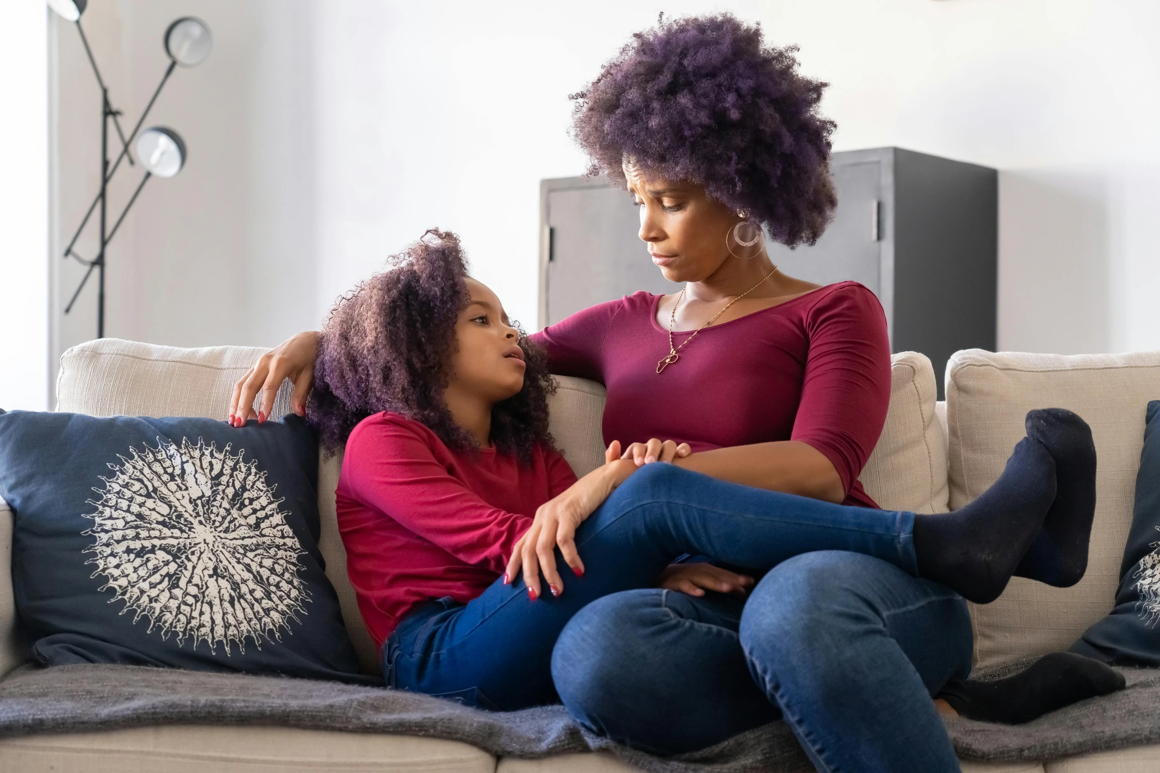 a woman sitting on top of a couch next to a young girl, pexels, dark purple skin, multiple stories, afro hair, supportive