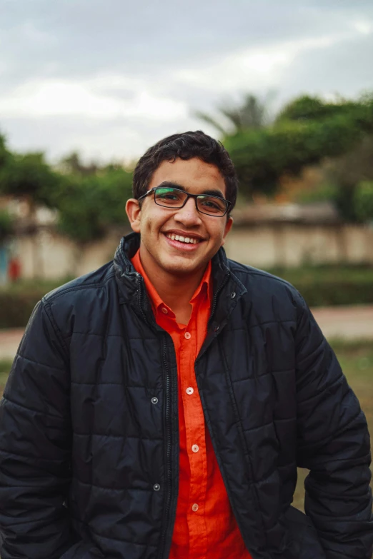 a man in an orange shirt and black jacket, by Ahmed Yacoubi, cute slightly nerdy smile, egyptian, high school, outdoor photo