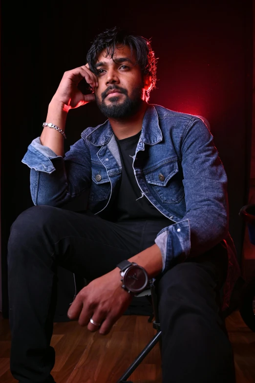 a man sitting in a chair talking on a cell phone, an album cover, pexels, hurufiyya, a portrait of rahul kohli, wearing a jeans jackets, studio potrait, night time