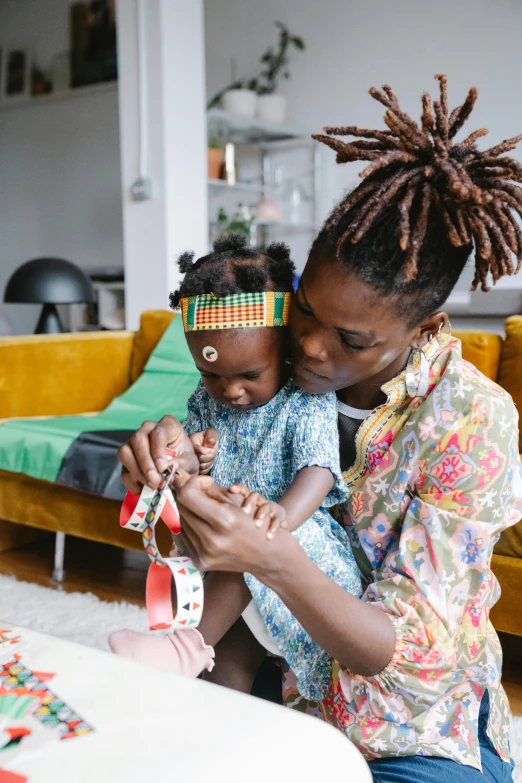 a woman sitting on a couch holding a baby, pexels contest winner, black arts movement, short dreadlocks with beads, kids toys, vibrant patterns, willow smith young