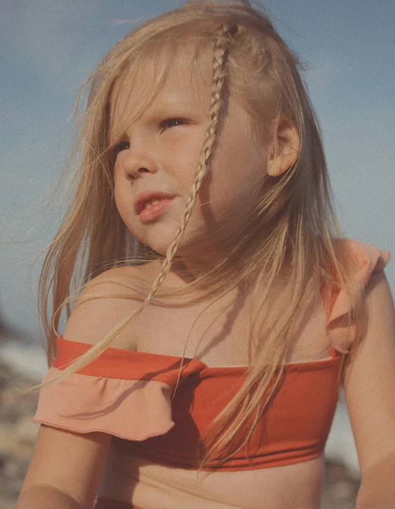 a little girl sitting on top of a sandy beach, an album cover, unsplash, incoherents, orange braided hair, in retro swimsuit, close-up portrait film still, aurora aksnes
