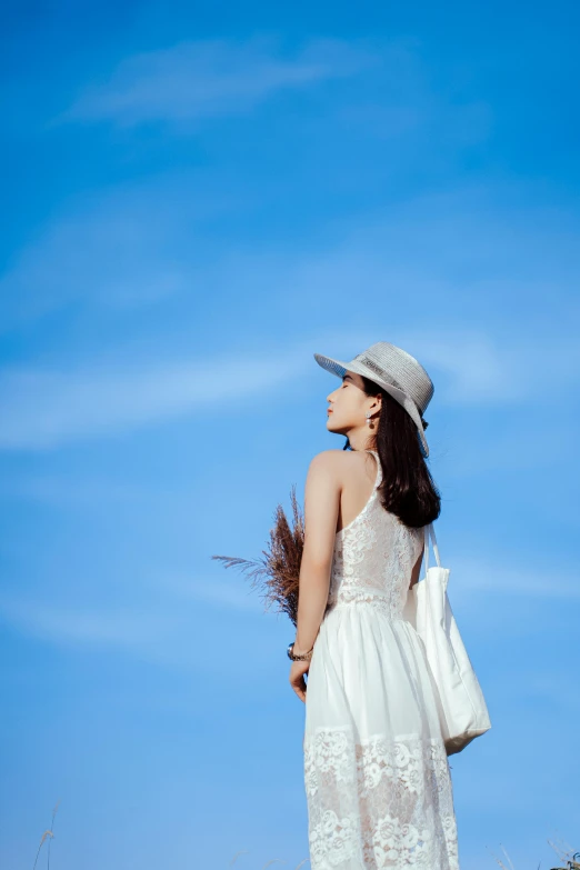 a woman in a white dress and hat standing in a field, by Tan Ting-pho, unsplash, minimalism, cloudless blue sky, 5 0 0 px models, looking up into the sky, cinematic outfit photo