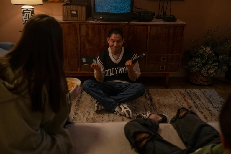 a group of people sitting on the floor in a living room, a picture, inspired by Liam Wong, holding pizza, [ theatrical ], medium shot of two characters, hollywood promotional image