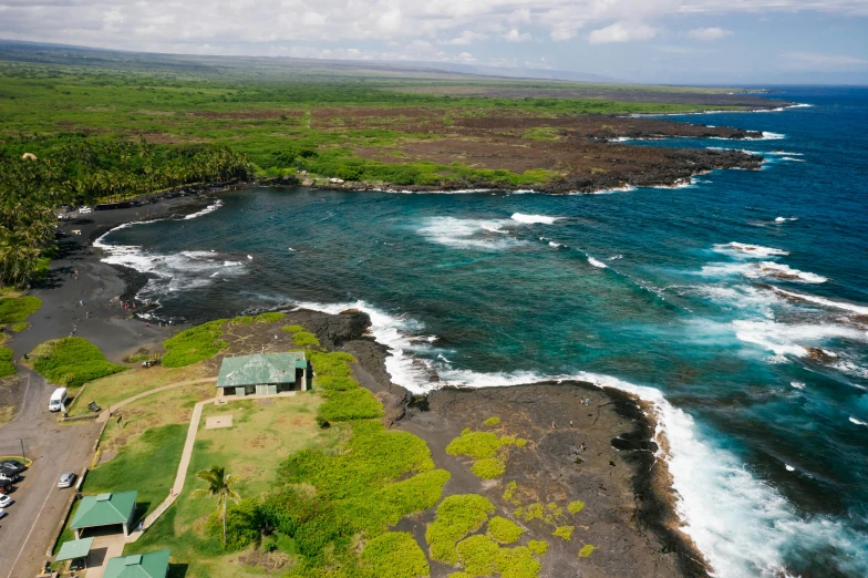 a large body of water next to a lush green hillside, reefs, lava rock, small cottage in the foreground, aerial