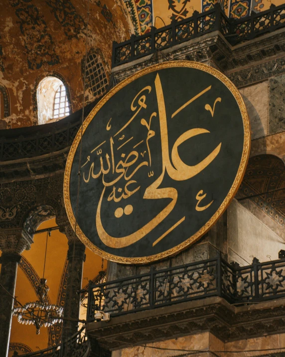 a clock mounted to the side of a building, an album cover, inspired by Osman Hamdi Bey, trending on unsplash, hurufiyya, mosque interior, calligraphy, interior of a marble dome, gold and black color scheme